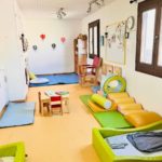 Salle d'activités avec mobilier enfants, tapis de motricité et décoration ballons